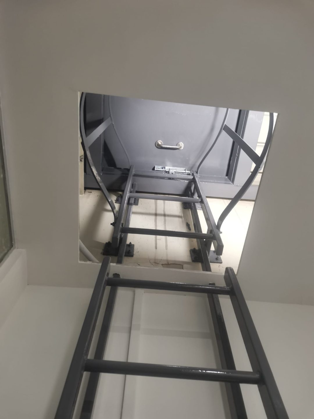 Cat ladder rising into the open roof access panel from inside the Tuas View building