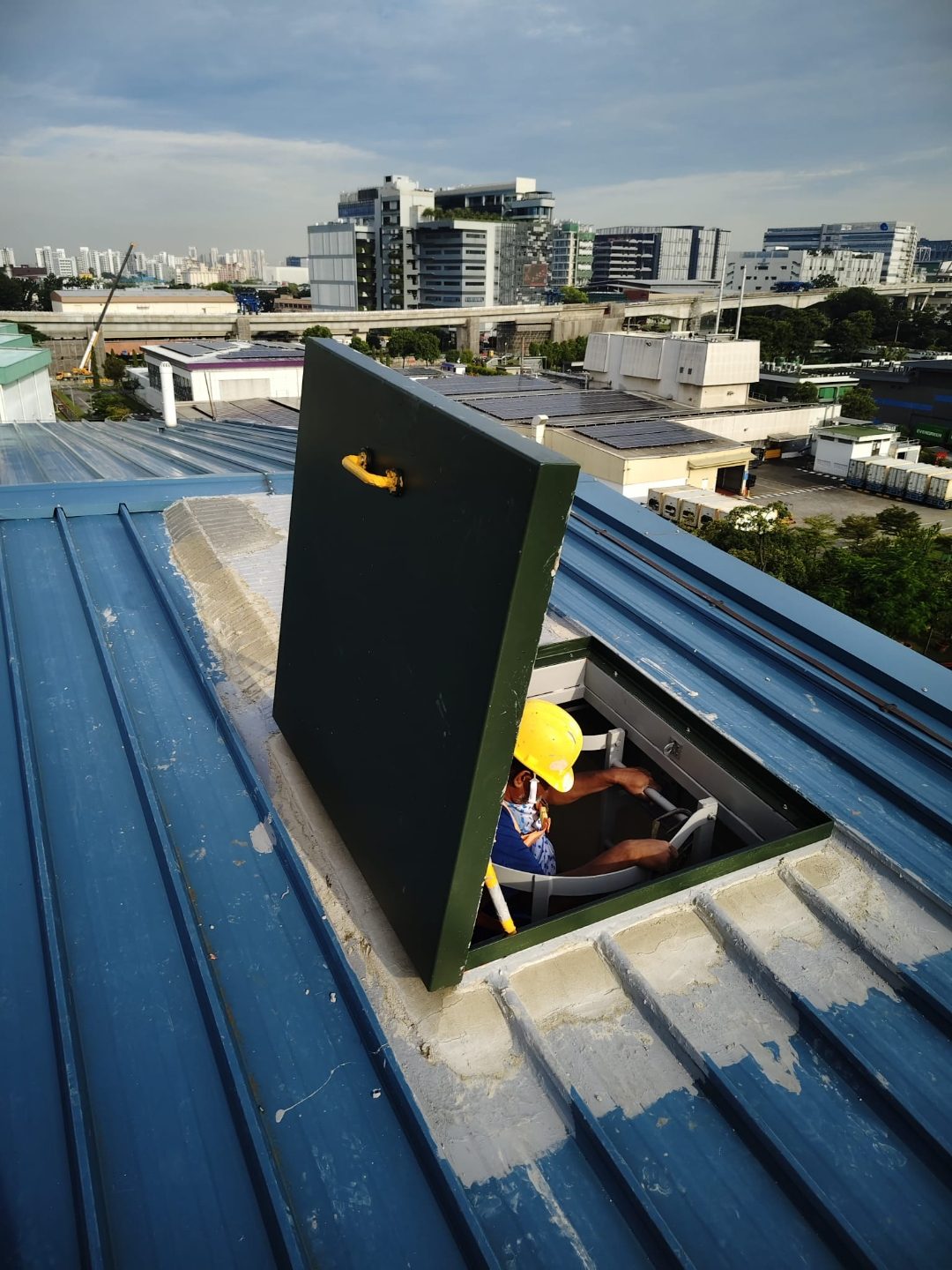 Roof access hatch panel installed on the metal-deck roof at Wan Lee with worker visible at the opening