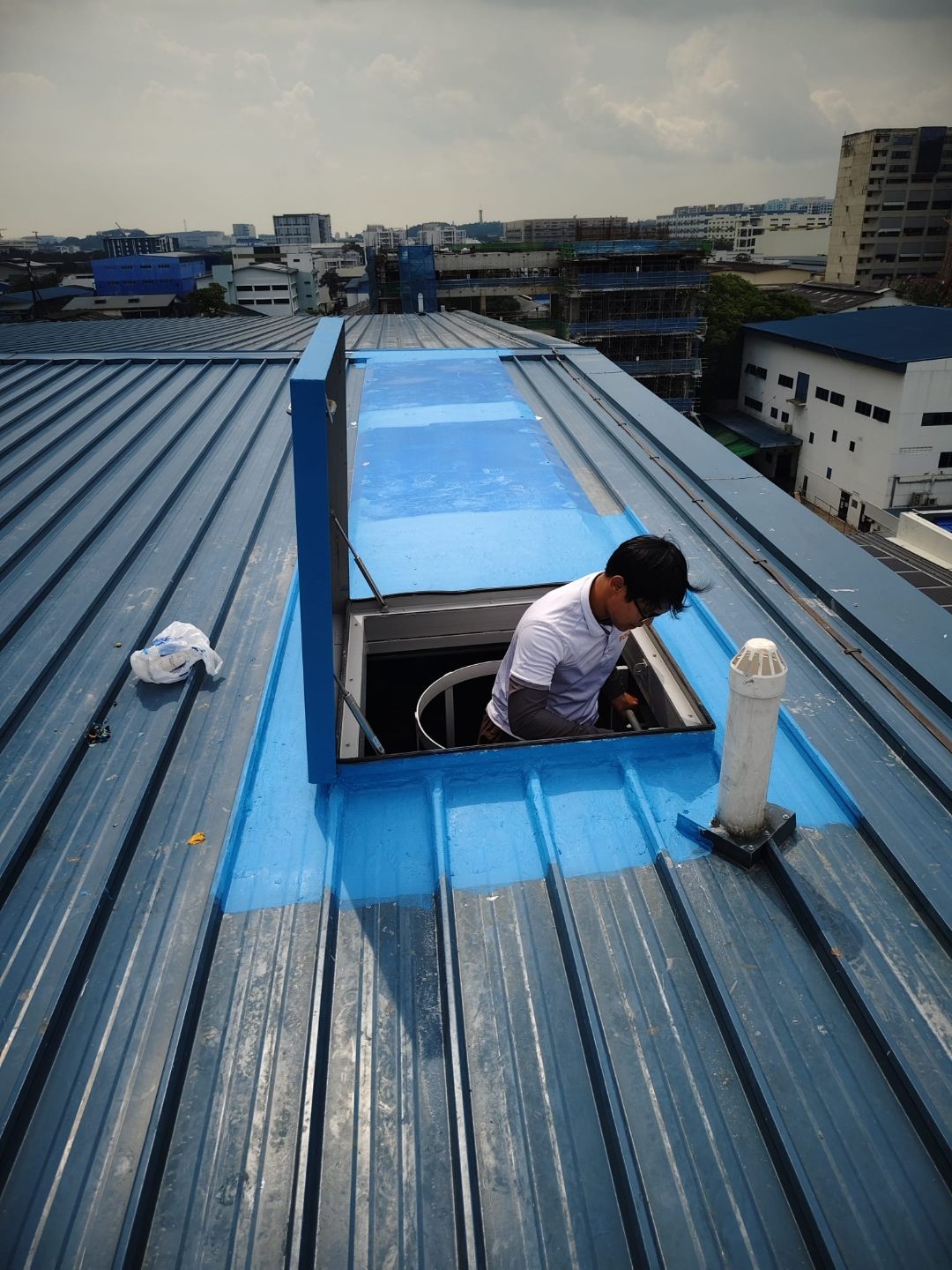 Roof-level view of the open access hatch at Wan Lee with worker emerging onto the metal-deck roof